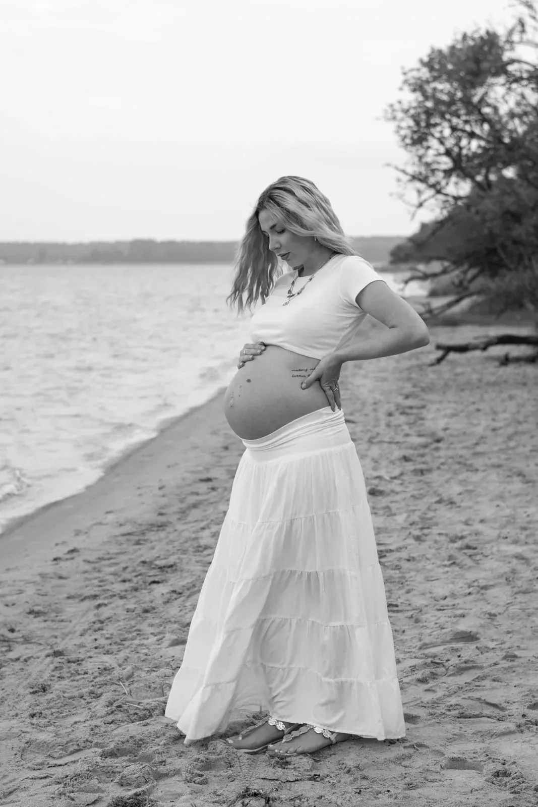 Schwarzweißbild: Schwangere am Strand, die Hände unter dem Babybauch