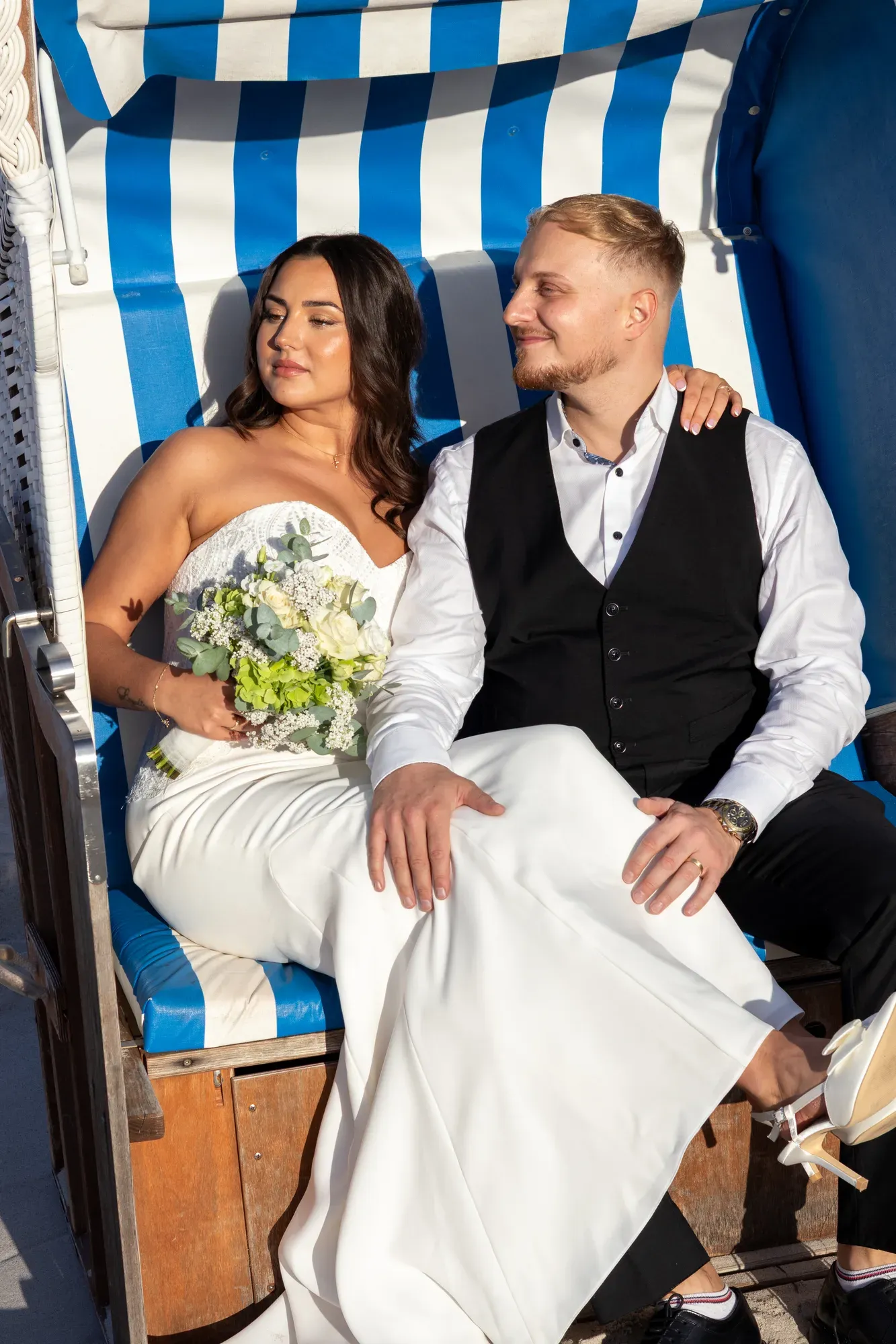 Brautpaar sitzt lachend in einem blau-weißen Strandkorb