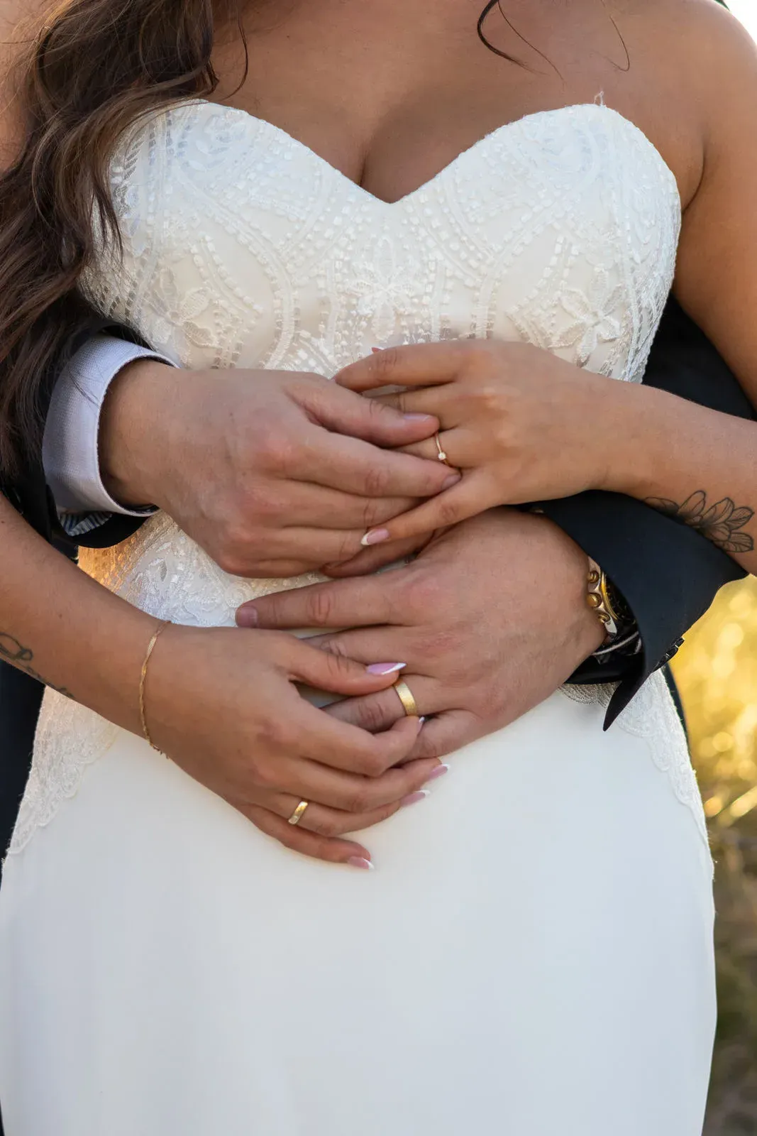 Hände des Brautpaares mit Ringen vor dem Brautkleid