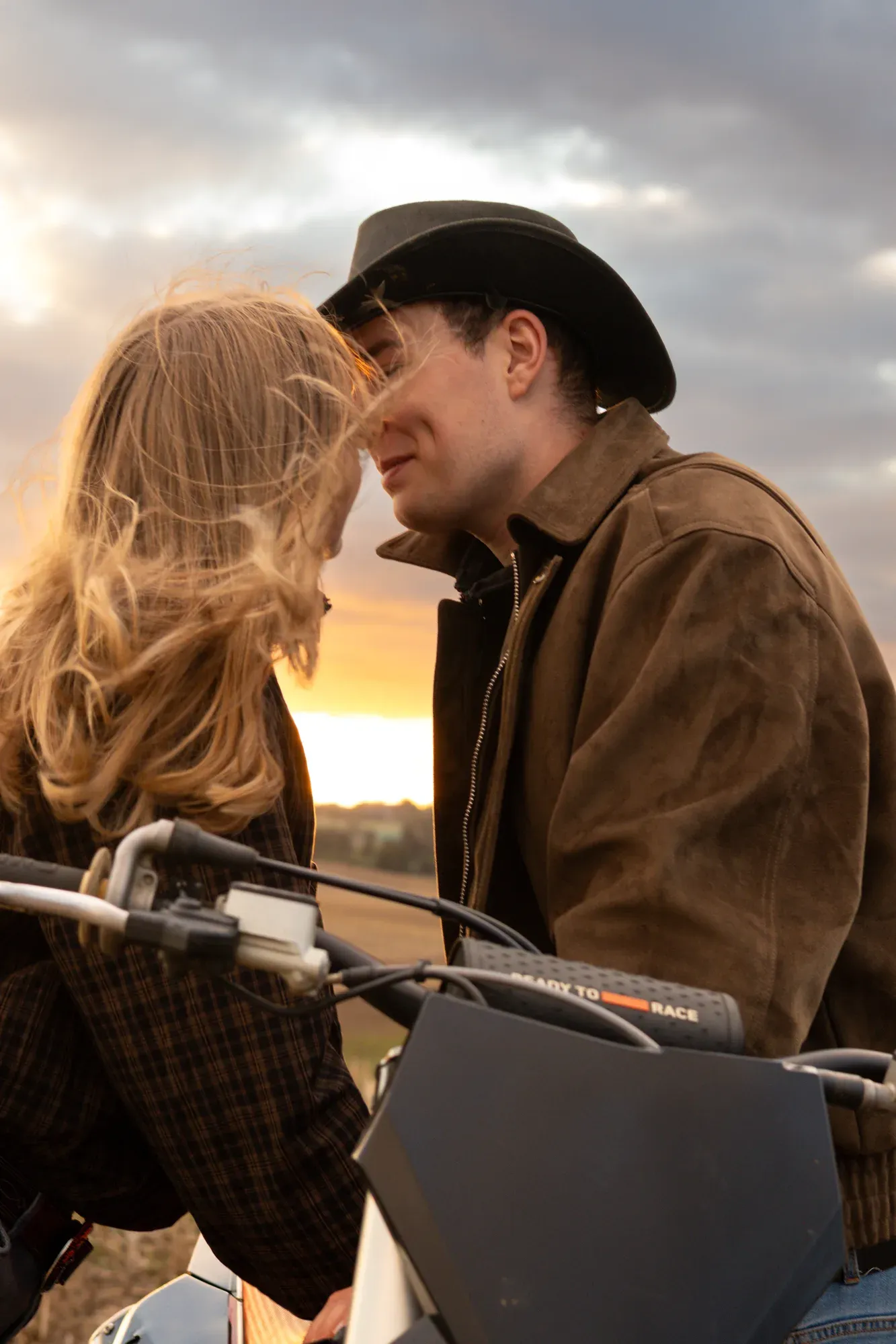 Paar mit Cowboyhut küsst sich auf dem Motorrad vor dem Sonnenuntergang