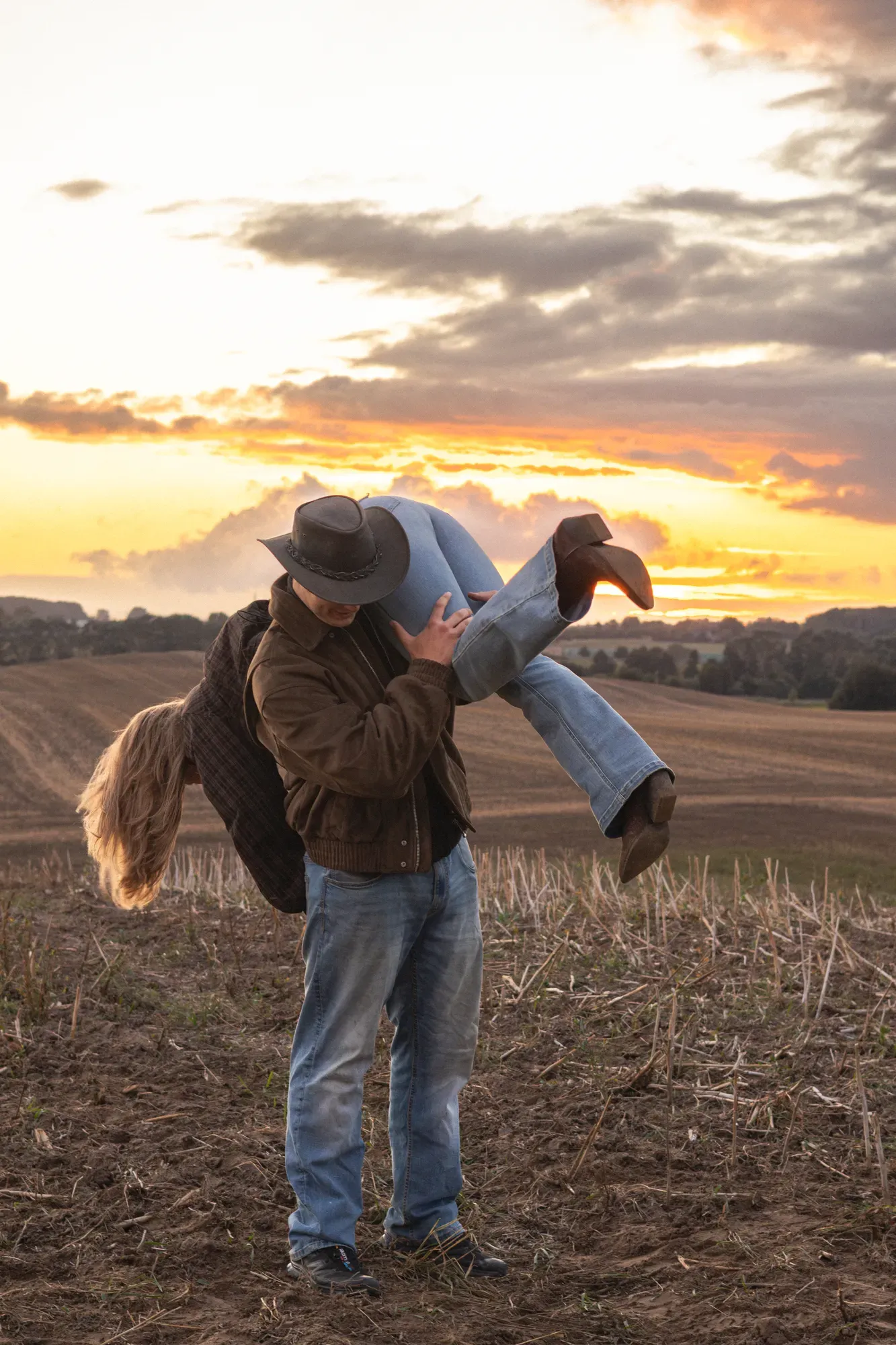 Mann hebt seine Partnerin bei Sonnenuntergang auf einem Feld hoch