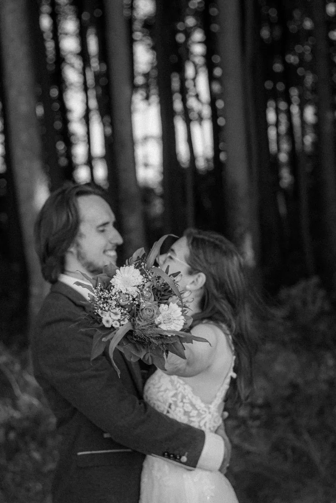 Schwarzweißbild: Paar umarmt sich mit Blumenstrauß im Wald