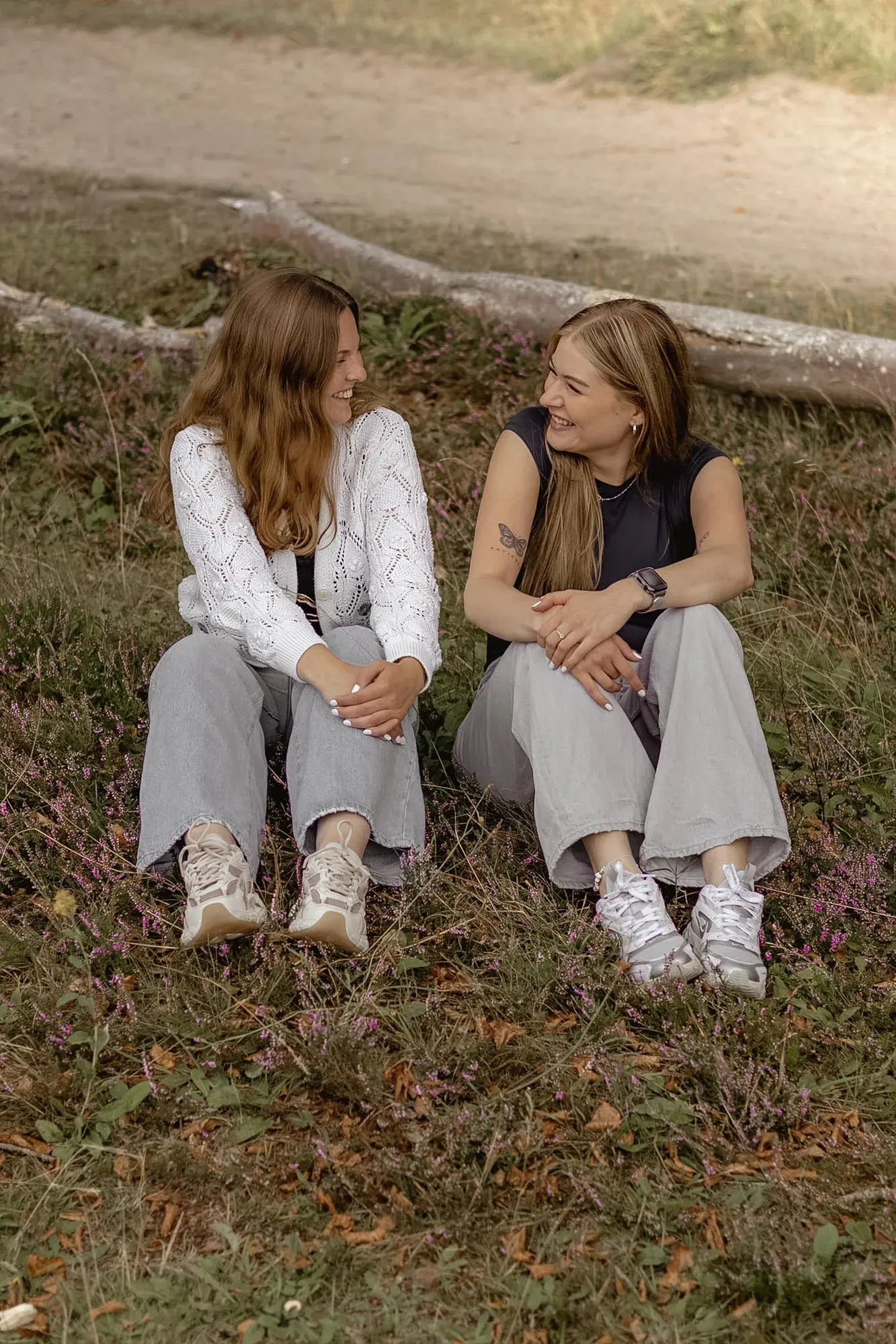 Zwei Freundinnen sitzen nebeneinander im Gras und lachen sich an