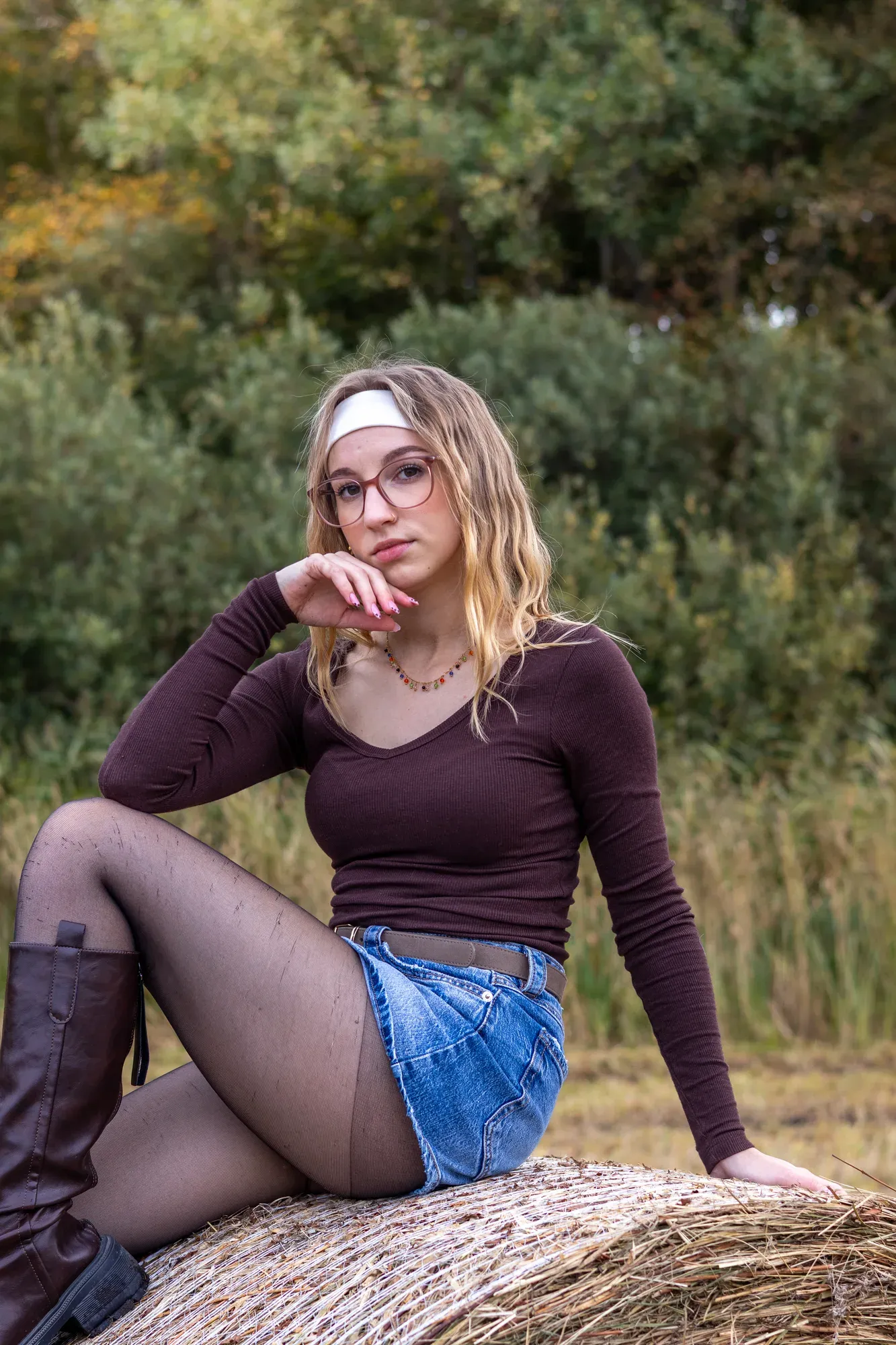 Frau mit Haarband und Brille sitzt auf einem Strohballen, die Hand am Kinn