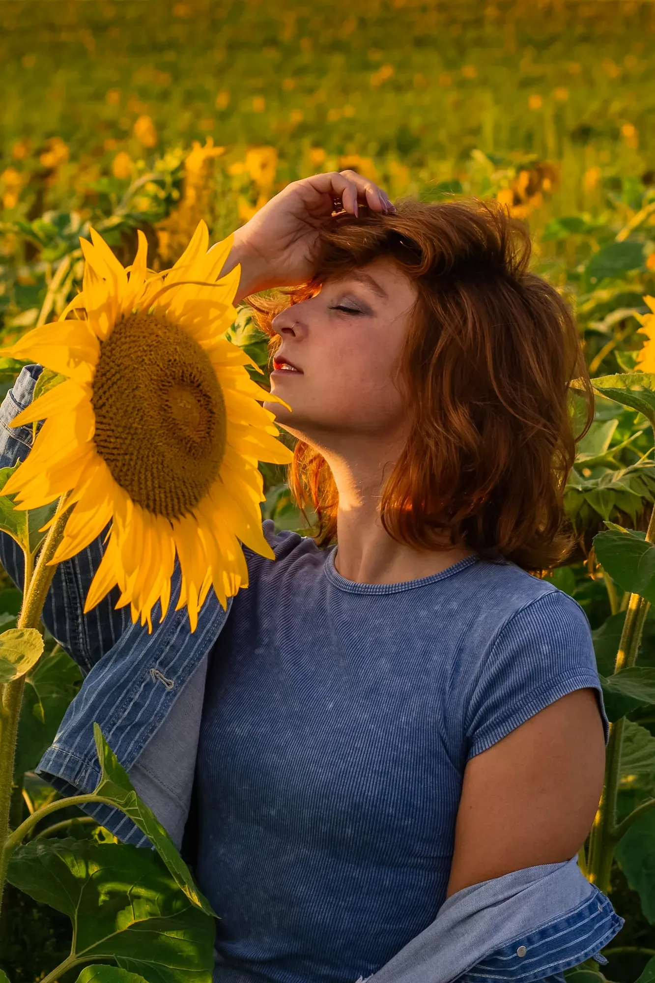 Frau mit geschlossenen Augen hält eine Sonnenblume im Sonnenblumenfeld