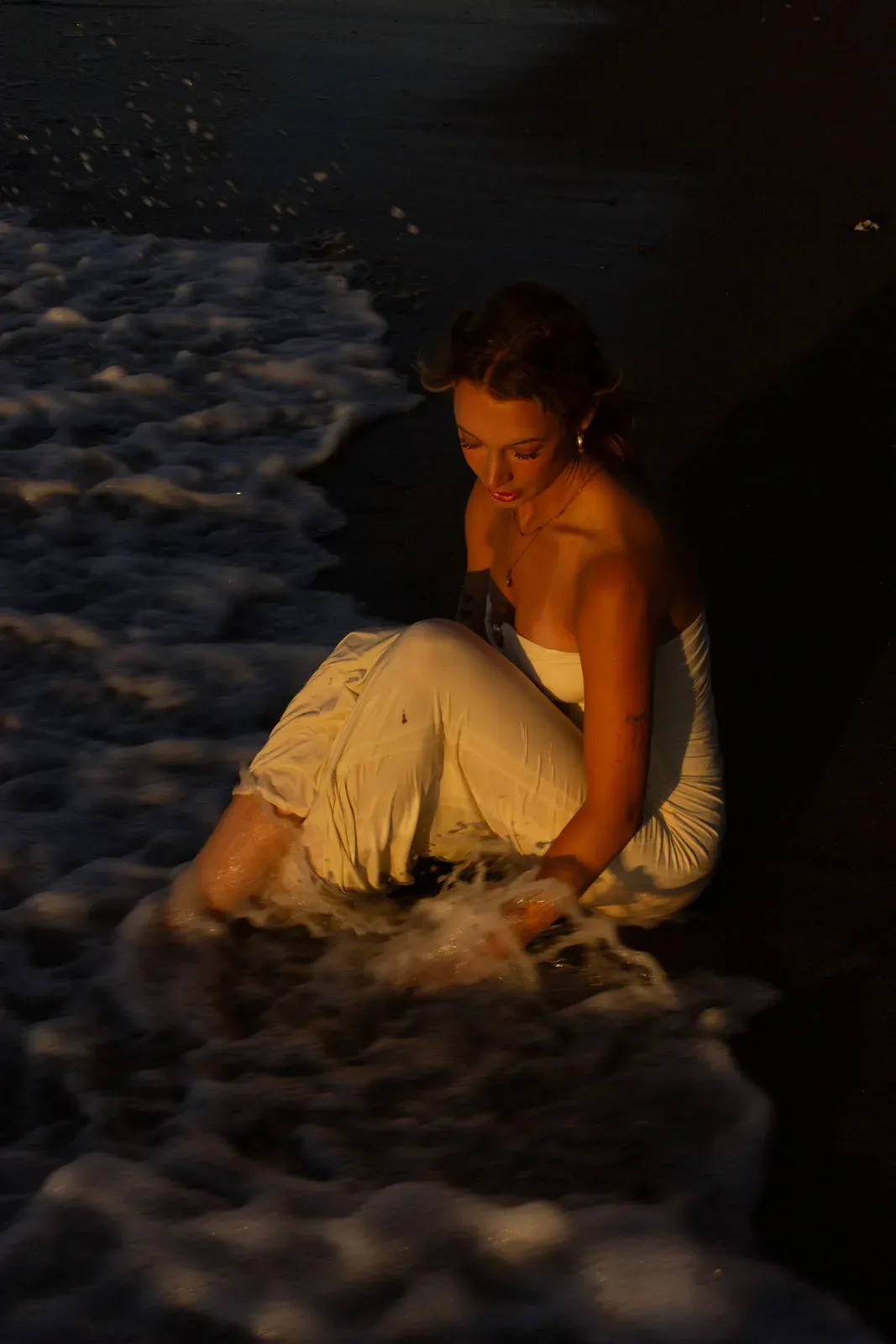 Frau in hellem Kleid sitzt im Wasser, Licht auf dem nassen Sand