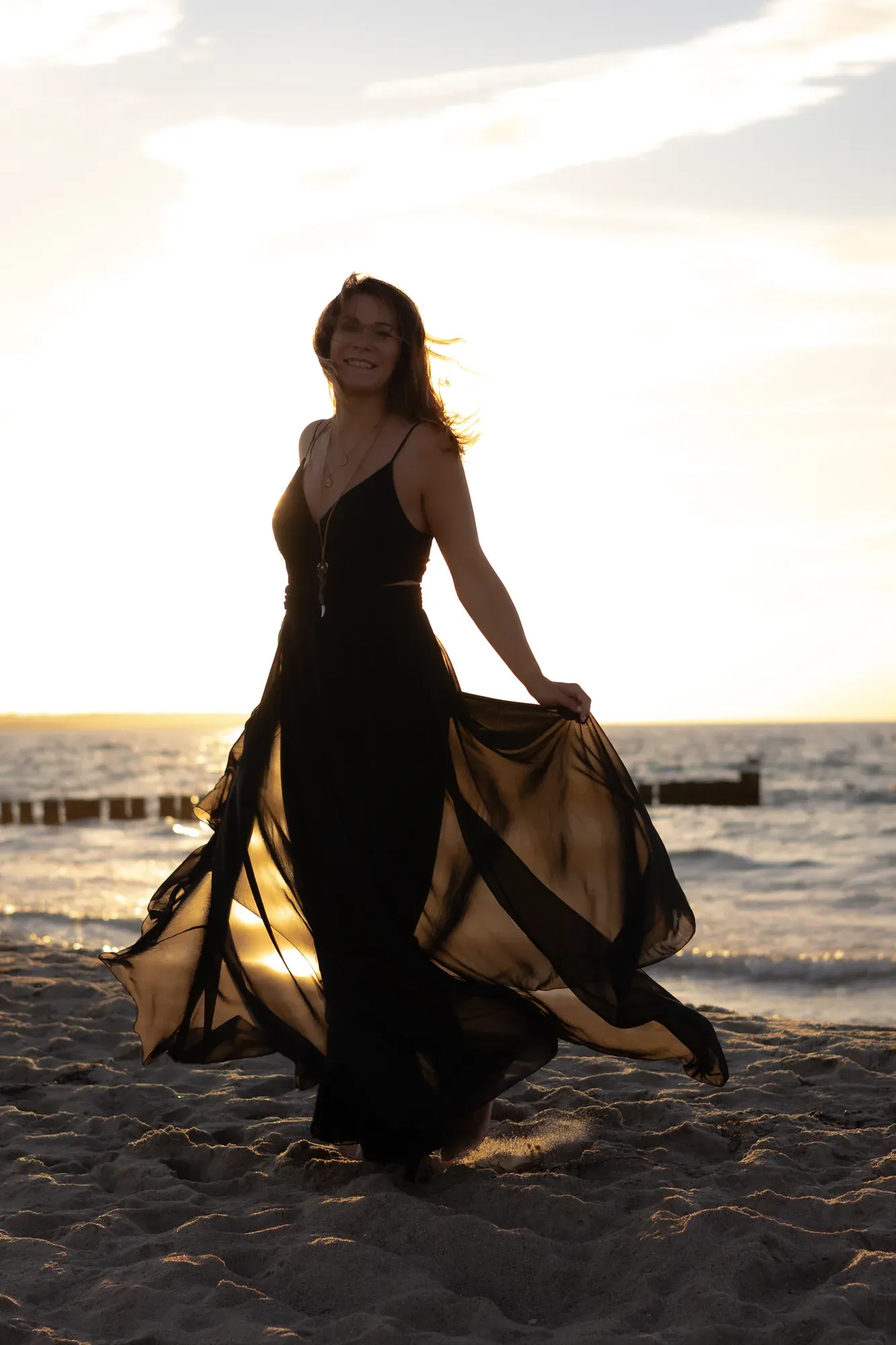 Frau breitet ihr schwarzes Kleid am Strand aus, die Sonne hinter ihr
