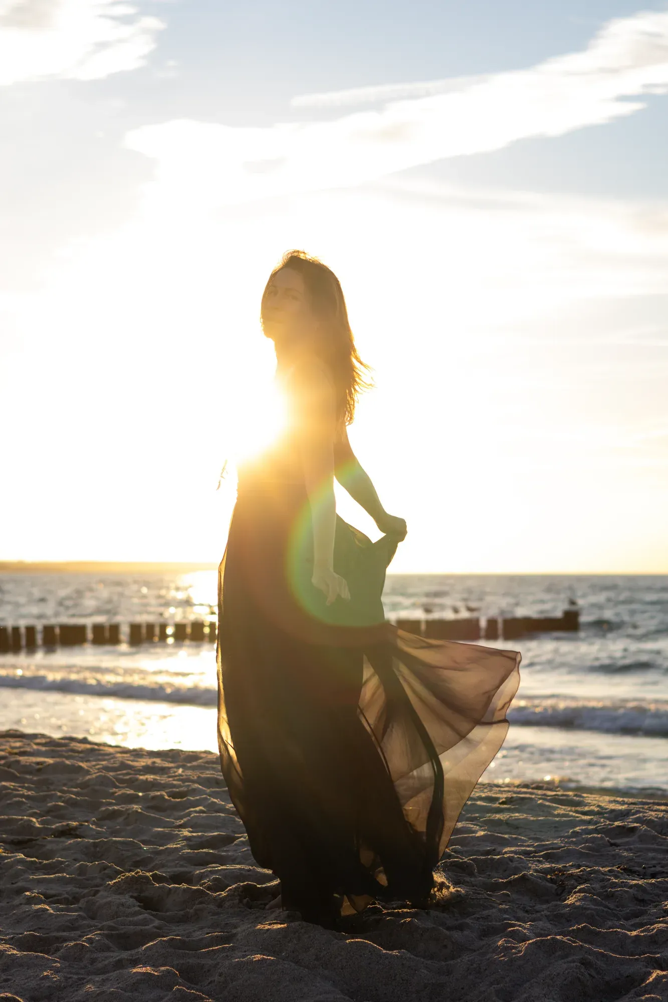 Frau im schwarzen Kleid dreht sich im Gegenlicht am Strand