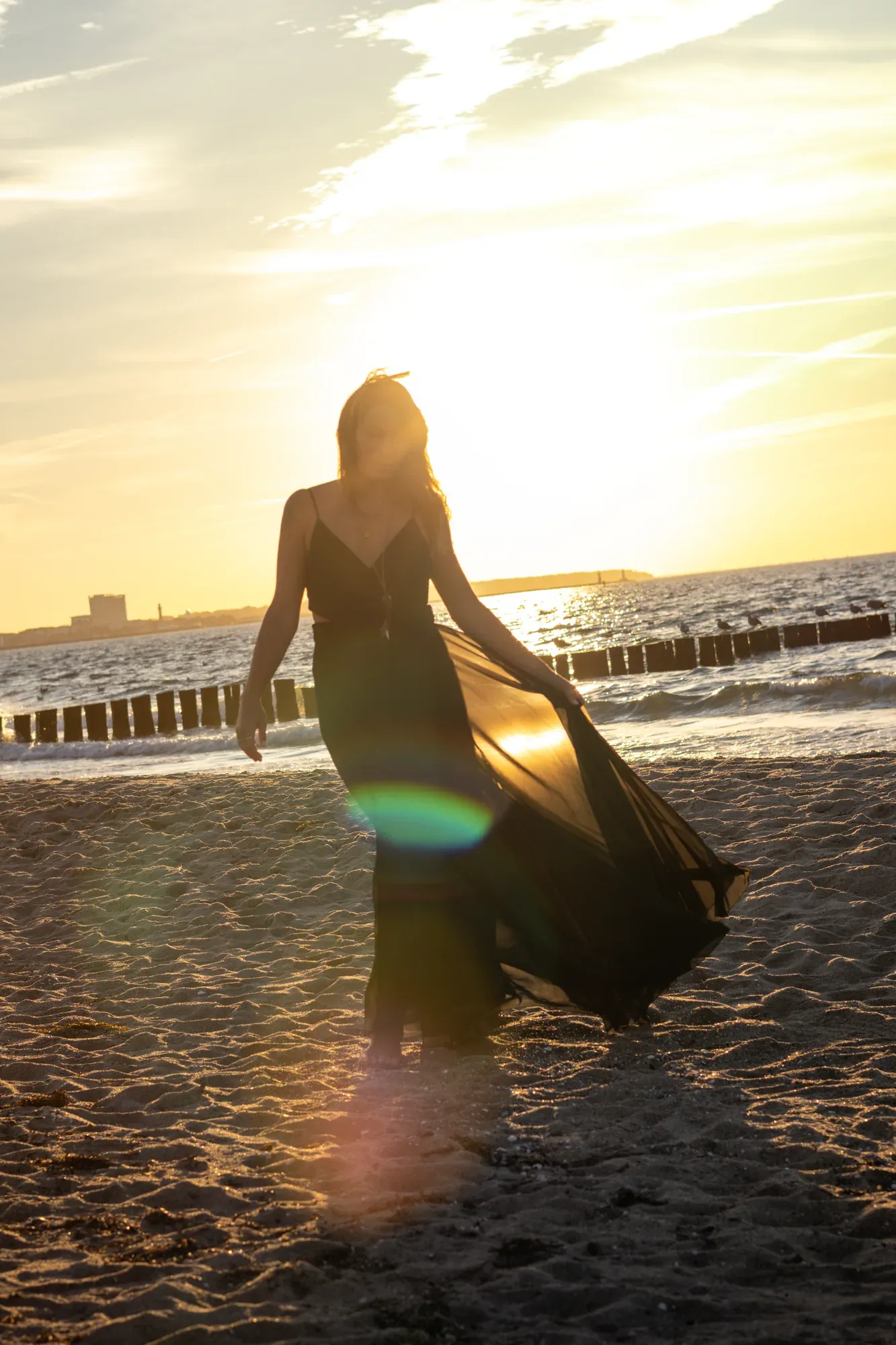 Frau schwingt ihr schwarzes Kleid am Strand vor der tiefstehenden Sonne
