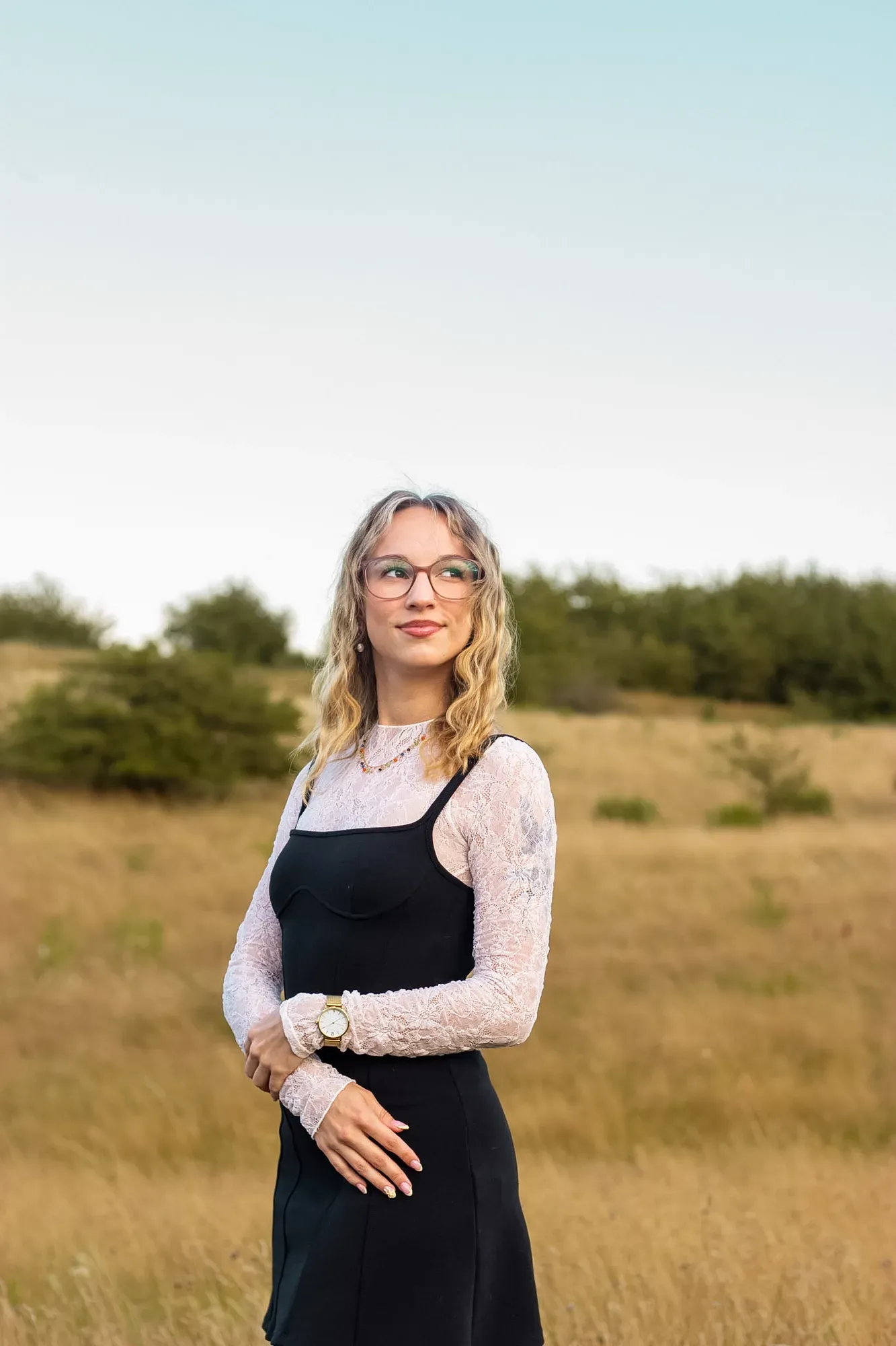 Frau mit Brille und schwarzem Kleid steht auf einer Wiese